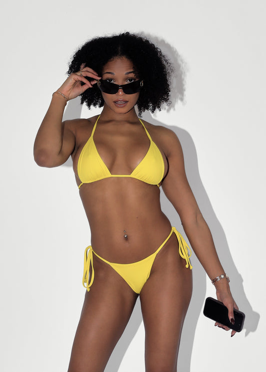 Woman in a yellow bikini posing against a white background